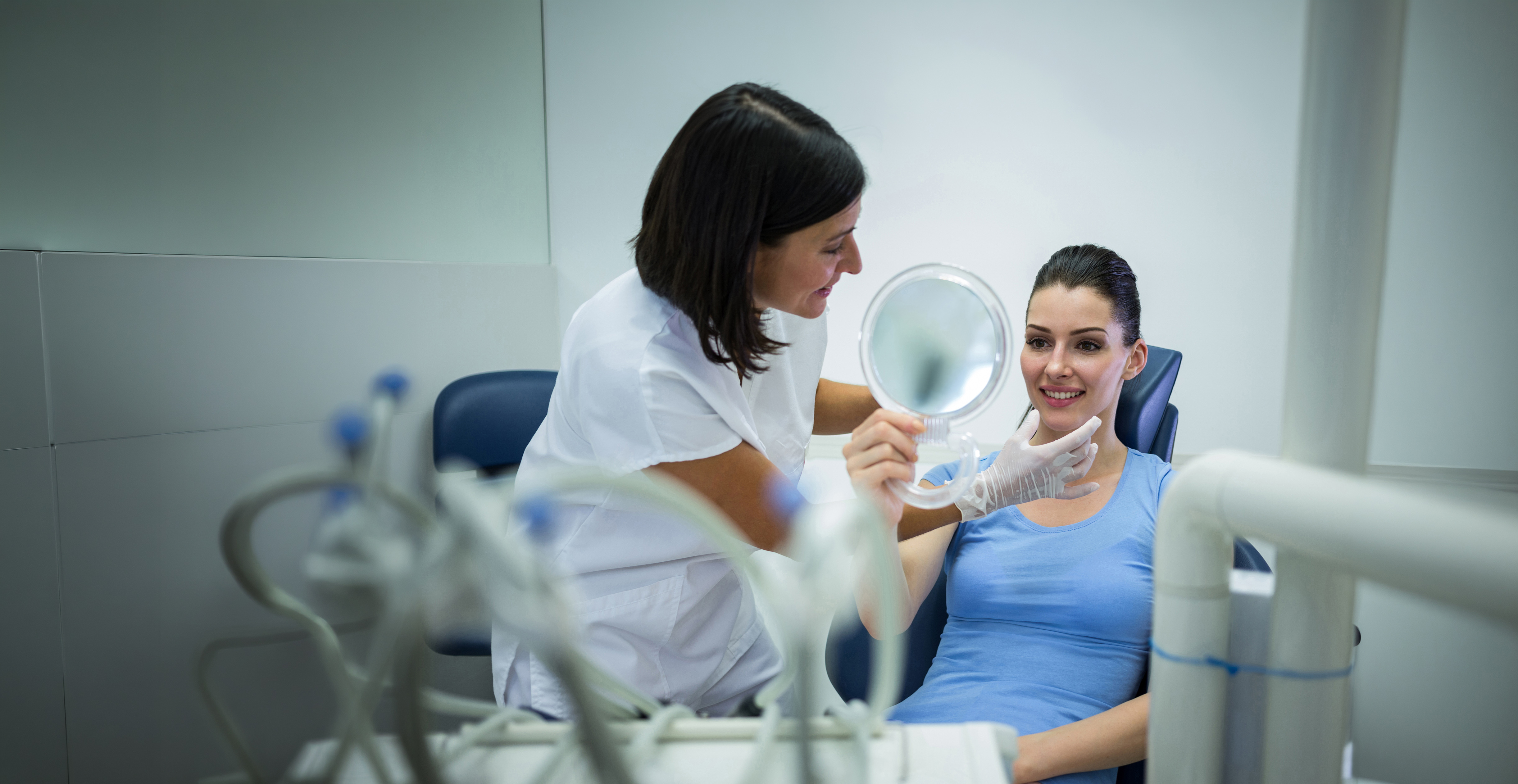 Dentista mostrando su sonrisa a una paciente con un espejo de mano.
